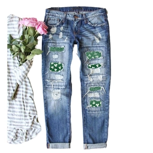 Women's straight blue ripped jeans featuring green shamrock patches and sequin details