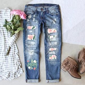 Close-up of distressed denim jeans with floral patches and MOM text embroidery detail