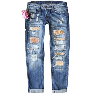 Women's blue ripped jeans with pink floral fabric patches and rolled cuffs on white background