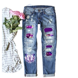 Women's blue distressed jeans with purple butterfly prints in a flat lay view