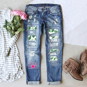 Flat lay of ripped denim jeans with floral patches and Super Mom print detail