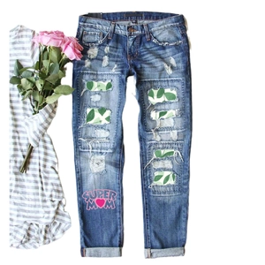 Women's light blue distressed jeans with green leaf patches and Super Mom print design