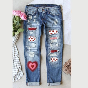 Détail d'un jean bleu vieilli avec des patchs cœur en paillettes rouges et des finitions déchirées