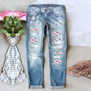 Women's blue distressed denim pants with American flag heart patches in a flat lay view