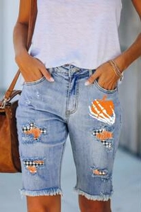 Detail of ripped blue denim shorts with Halloween pumpkin prints and plaid patches