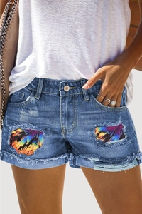 Dettaglio di pantaloncini di jeans blu con fori consumati e toppe in tessuto tie-dye colorato