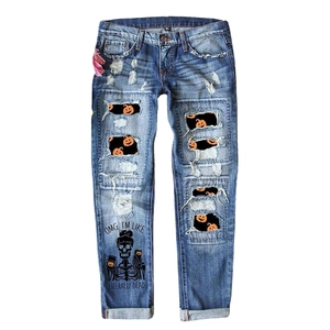 Distressed blue wash denim jeans featuring Halloween pumpkin prints and skeleton graphics