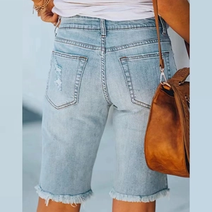 Detail of light blue denim shorts featuring distressed back pocket and frayed fringe hem