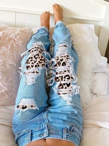 Détail d'un jean bleu clair taille haute avec empiècements imprimé léopard sous les trous