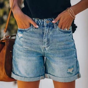 Detail of high waisted denim shorts with distressed ripped holes and rolled hem finish