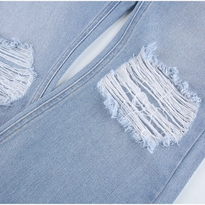 Macro detail of distressed denim showing frayed edges and white fiber rips on light blue jeans