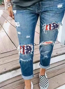 Detail of distressed denim jeans featuring USA flag patchwork and rolled cuff design