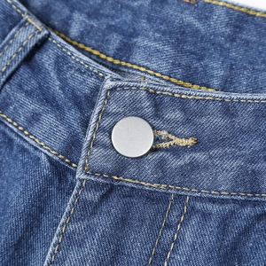 Détail macro du jean taille haute montrant le bouton en métal et les coutures jaunes