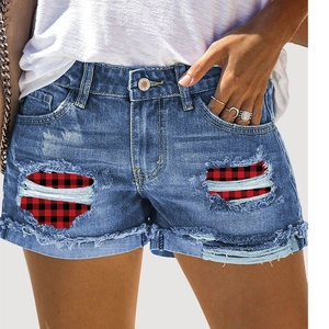 Detail of distressed denim shorts with red buffalo plaid patches and frayed raw hem edge