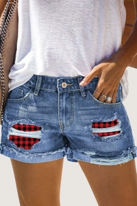 Detail of blue denim shorts featuring distressed holes with red and black plaid fabric lining