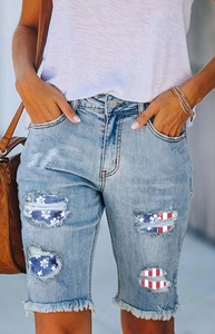 Close-up of denim shorts featuring American flag patches and frayed hem details