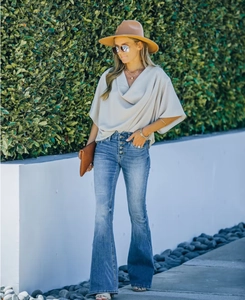 Detail of high-waisted flare jeans with button fly and beige draped neck short sleeve top