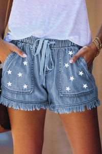 Detail of light blue denim shorts with star prints, frayed hems and drawstring waist