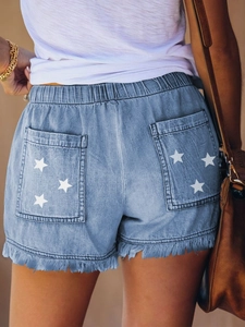 Detail of light blue denim shorts showing white star print on back pocket and raw hem fringe