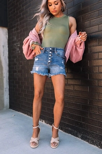 Detail view of high waist denim shorts with multi-button fly and frayed hems on a model