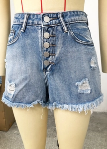 Detail of high waisted denim shorts featuring five button fly and distressed frayed edges