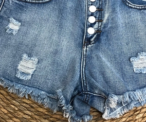Close-up of blue denim shorts with frayed raw hem and silver button fly detail