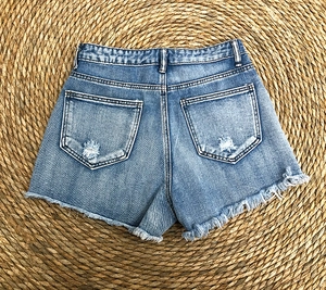 Detailed back view of blue denim shorts with ripped pockets and distressed raw hem edges