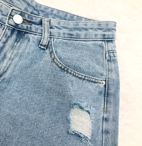 Gros plan détaillé d'un short en jean bleu clair avec déchirures et bouton JEANS en métal
