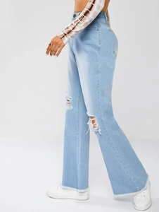 Detail of ripped light blue flared jeans showing distressed denim and frayed hem