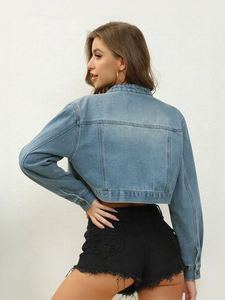 Detail of light blue cropped denim jacket with raw hem black shorts and metal buttons