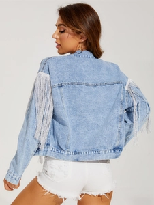 Detail shot of long silver fringe on the sleeves of a light blue washed denim jacket