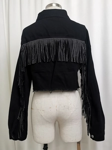 Close-up of black denim jacket back featuring silver rhinestone fringe and raw hem edge