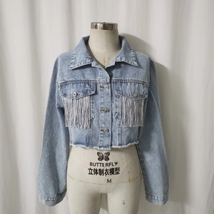 Dettaglio della giacca di jeans azzurra con nappe argentate e orlo a taglio vivo