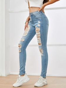Detail of high waisted light blue skinny jeans featuring distressed ripped knees and raw hems