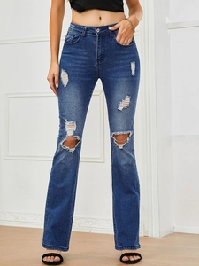 Close-up of distressed denim texture with ripped details on dark blue flared jeans