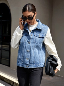 Close-up of blue washed denim vest with metal buttons over a white ribbed knit sweater