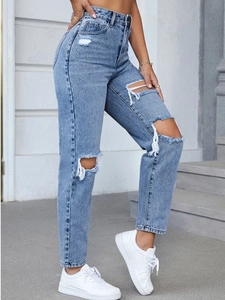 Detail of high-waisted distressed light blue denim jeans showing ripped knees and hem