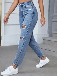 Detail of high waisted distressed blue jeans featuring ripped knees and frayed edges