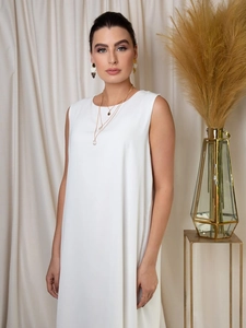 Gros plan du décolleté de la robe blanche sans manches avec bijoux dorés superposés