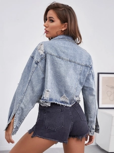 Close-up of distressed ripped details and raw hem on a light blue cropped denim jacket