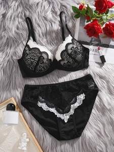 Detailed flat lay of black floral lace lingerie set with white scalloped trim and rose