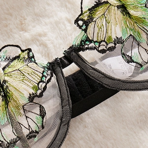 Detailed embroidery of green floral patterns on white mesh lace lingerie with black straps