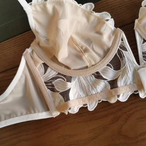 Detail of white floral lace embroidery and underwire support on a sheer mesh bra