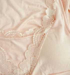 Close-up of delicate white lace trim on a soft light pink modal nightdress fabric