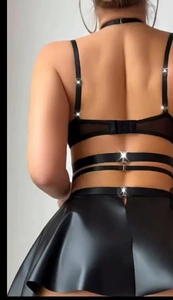 Detail van zwarte faux lederen minirok en strappy open rug top met metalen gespen
