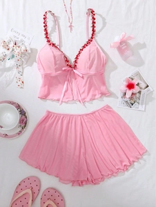 Flat lay of pink pajama set with floral embroidery and bow tie detail on white background