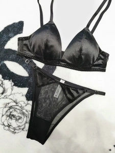 Detail of black satin lingerie set with lace trim and size label on white carpet