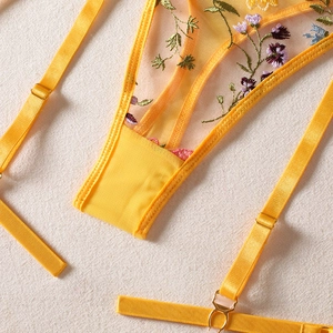 Close-up of floral embroidery on yellow sheer mesh lingerie with gold metal buckles