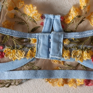 Detail view of double row back hooks and floral embroidery on a sheer lace bra