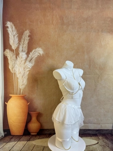 Détail d'un ensemble de lingerie blanc avec chaînes dorées sur mannequin et fond rustique